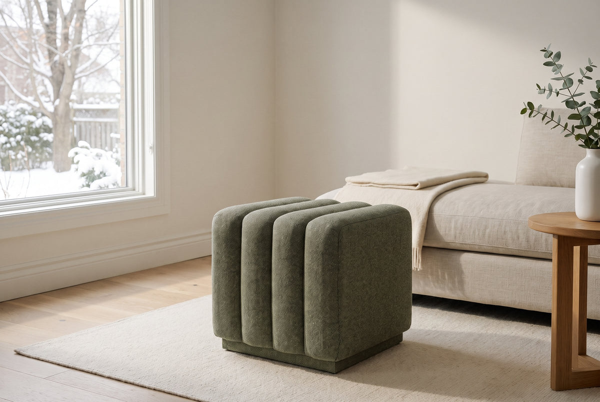 Abbadia ottoman in moss on a cream wool rug beside a linen sofa in an Ottawa living room, a snowy garden through the window