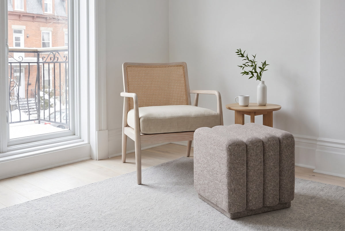 Abbadia ottoman in stone on a light grey rug beside a cane armchair in a Montreal Plateau reading corner