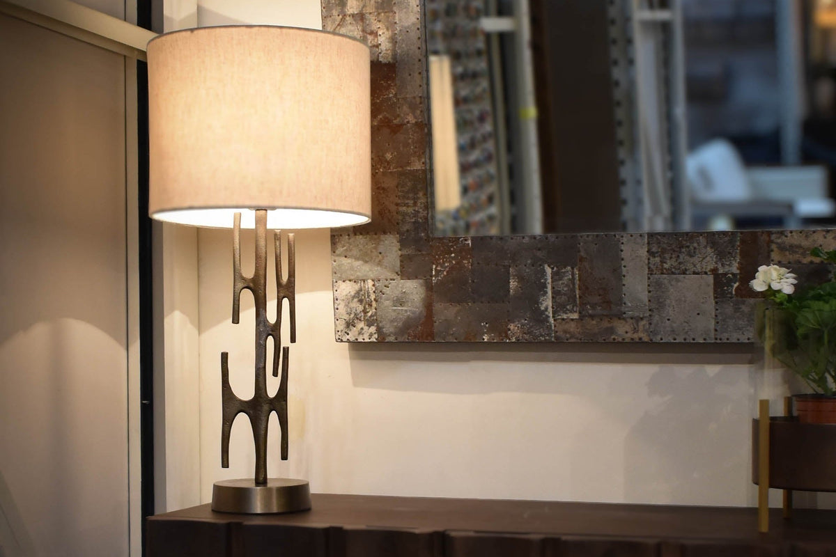 Adeline brass table lamp lit on a dark wood sideboard beside a mirror