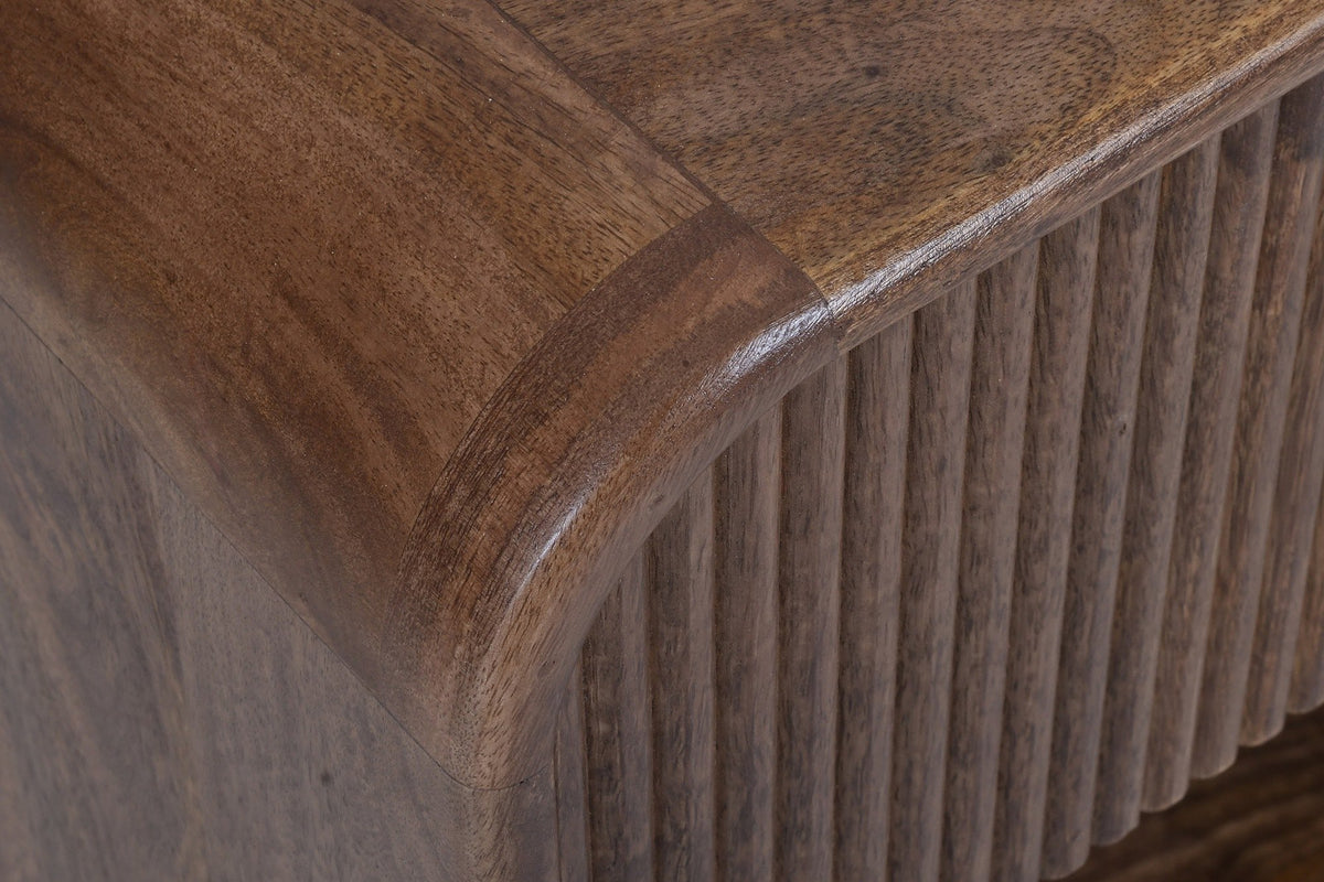 Close-up of the Alberona corner in walnut: the rounded bend of the top over the reeded drawer front, solid mango grain