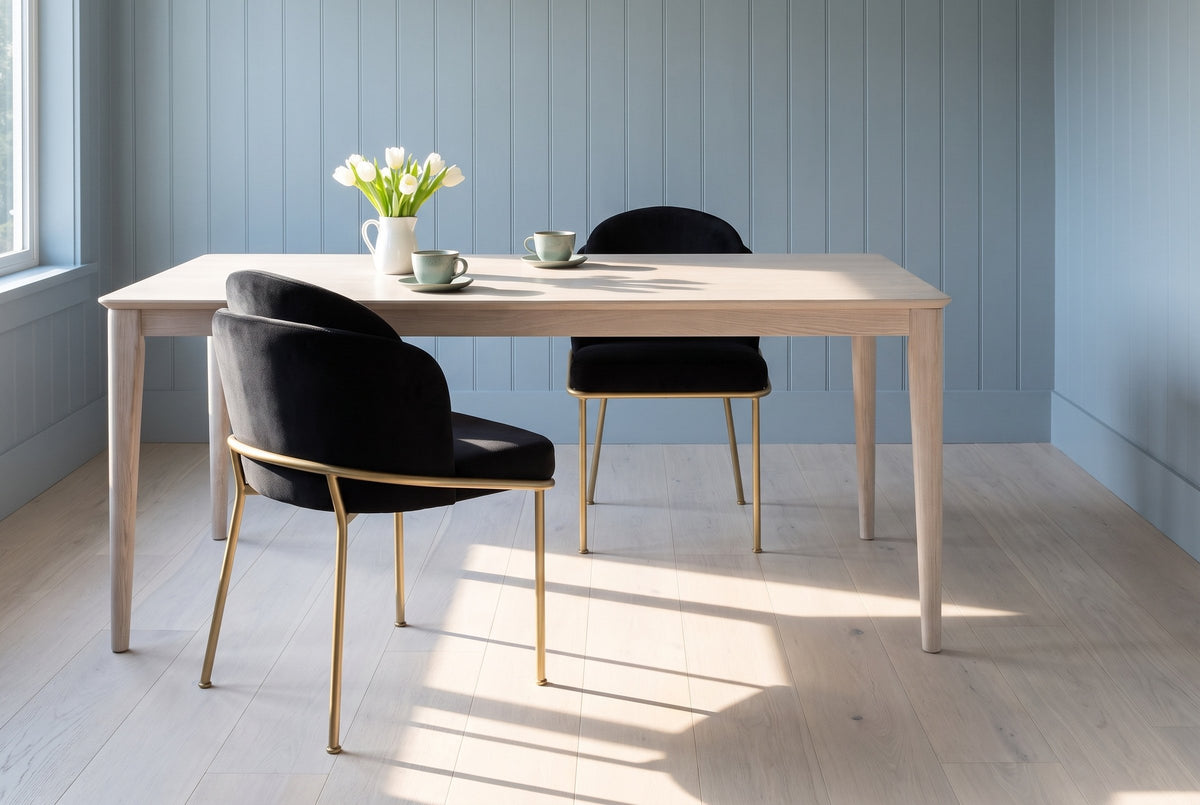 Two Alexander black velvet dining chairs with brass legs at a pale ash table with celadon cups and white tulips, against powder blue-grey panelled walls in morning light