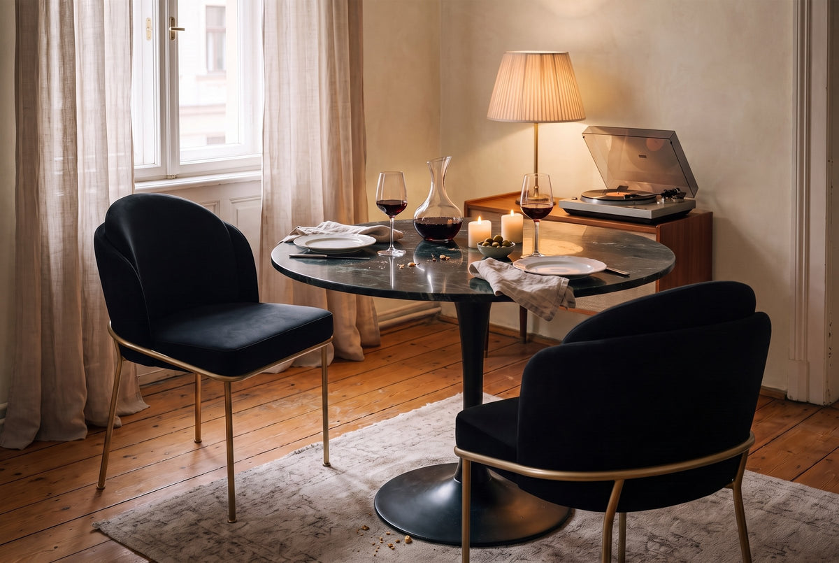 Two black velvet Alexander dining chairs at a green marble table set for two in a Vienna apartment, a record player and lamp behind