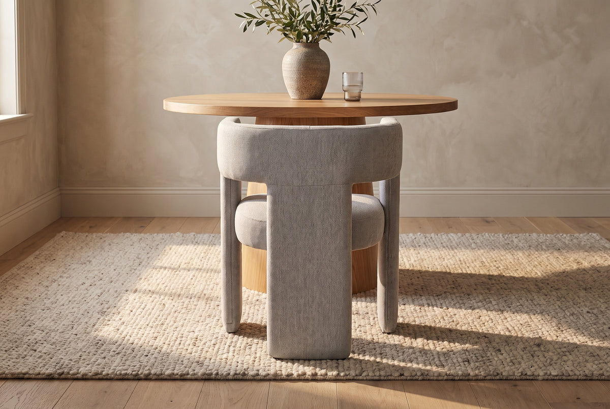 Andrea light grey woven fabric dining chair seen from behind at a round oak pedestal table in warm sunlight