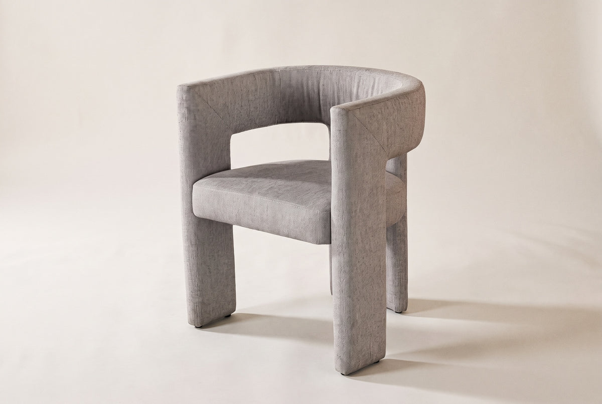 Andrea light grey woven fabric dining chair in three-quarter side view on an off-white studio backdrop