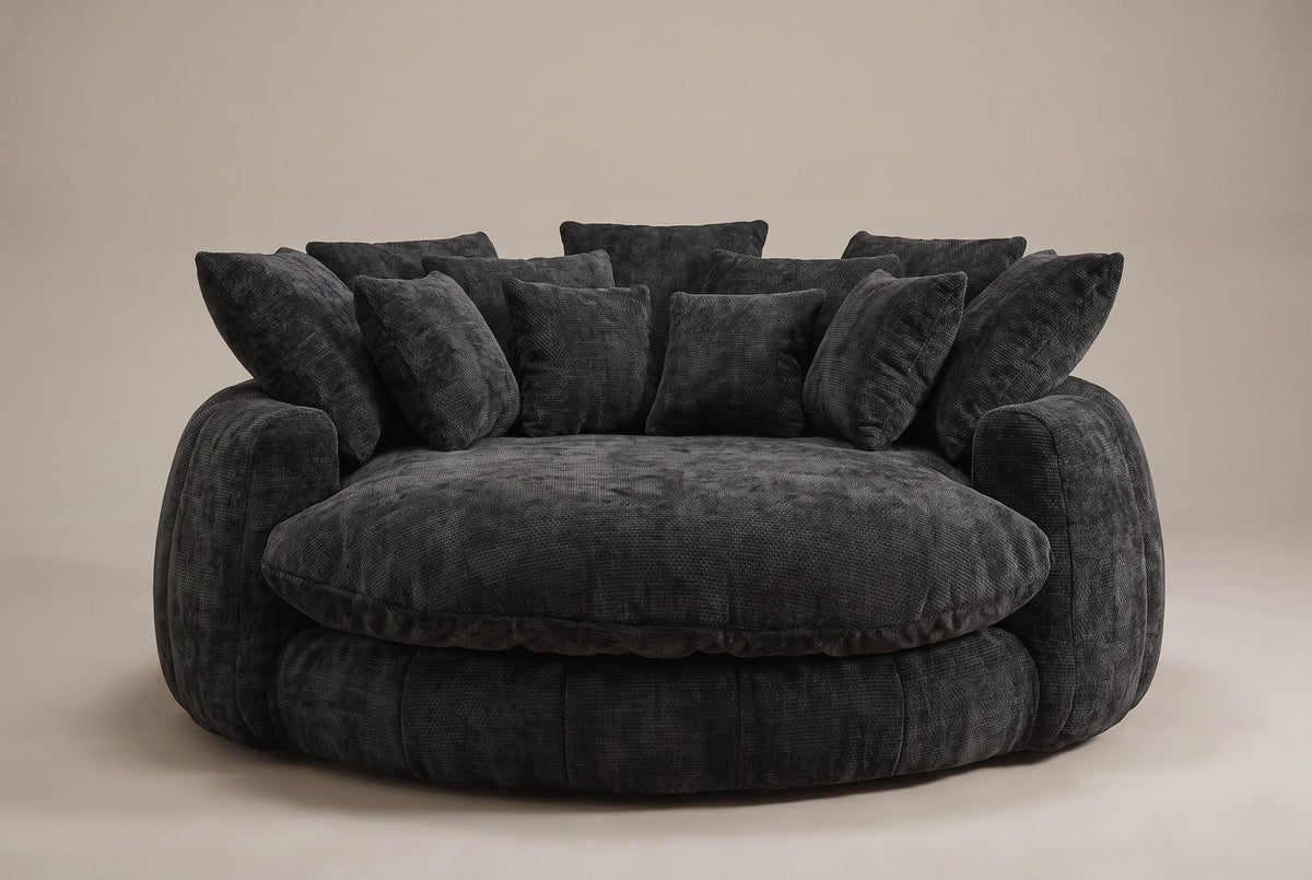 Aosta lounge chair in black, straight front view: one thick round seat cushion inside a low channelled ring, square pillows along the back