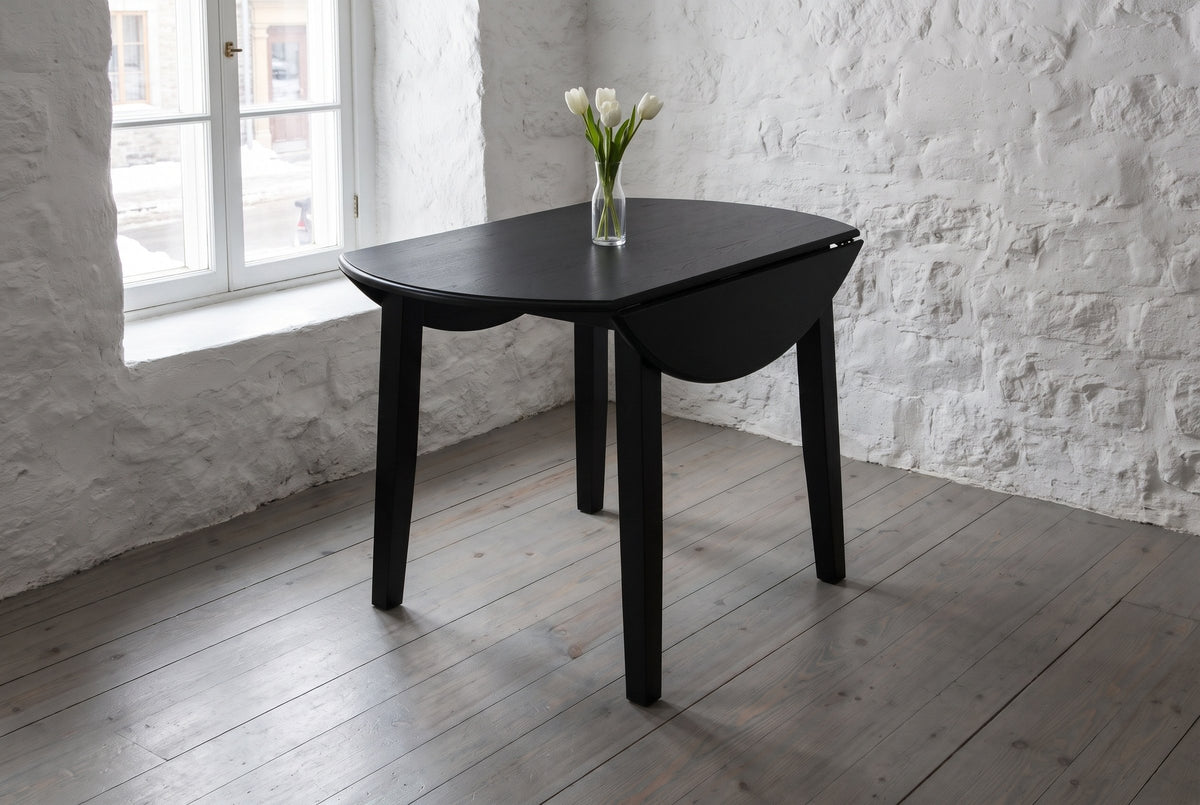 Arden drop-leaf dining table in Black with both leaves down and a vase of white tulips, in a whitewashed stone house in Quebec City, snow outside