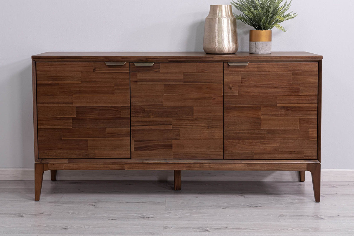 Ashby acacia 3-door sideboard in Natural Brown against a pale wall with a brass vase
