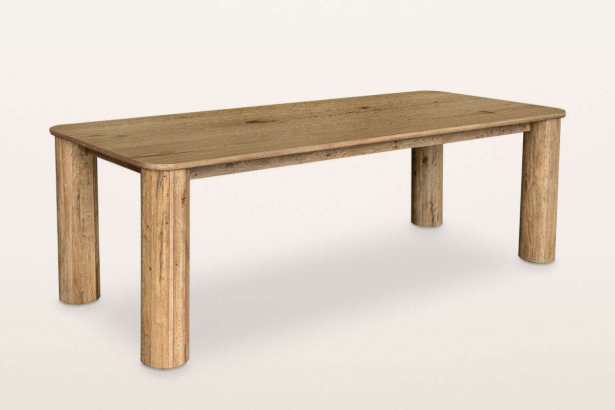 Atzara oak dining table in Natural, three-quarter view on a warm white studio backdrop: a long top with rounded corners on fo