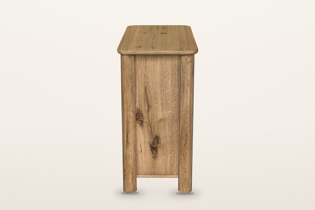 Atzara Small sideboard in Natural, end view on a warm white studio backdrop: a flat oak end panel between two round column po