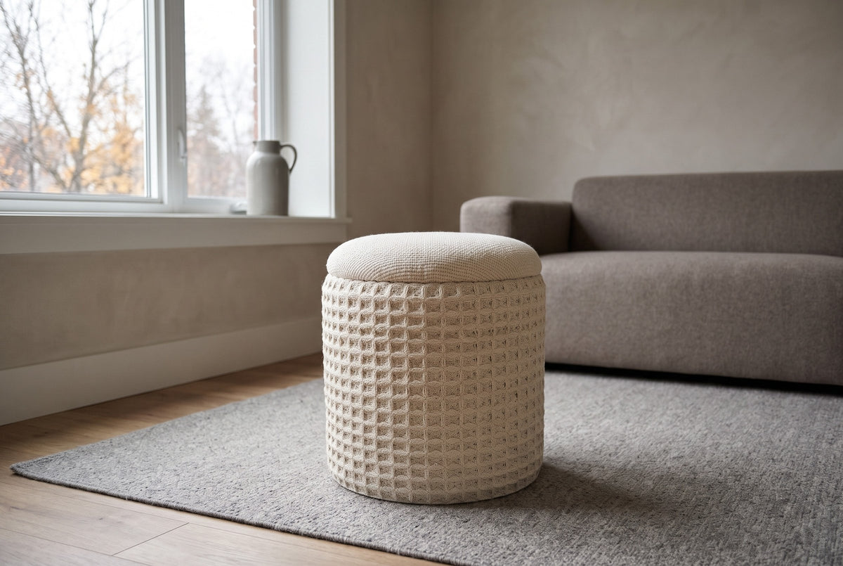 A Balme pouf in Ivory on a stone-grey wool rug in a brick house living room in the Glebe, Ottawa, a taupe-grey wool sofa behind and bare trees through the window