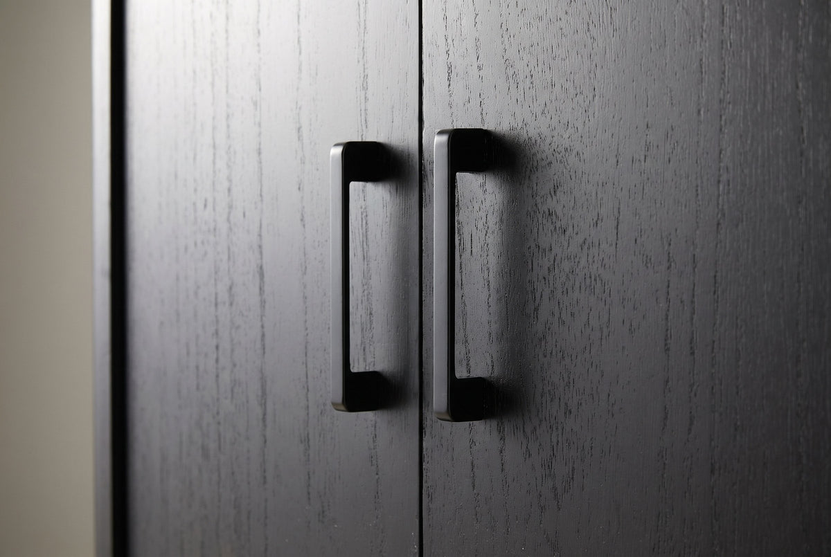 Close-up of two matte black metal bar pulls at the meeting edge of two black-stained wood veneer doors