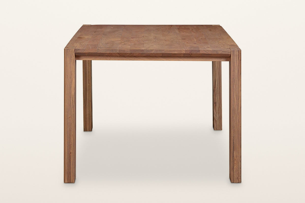 End view of the Bominaco dining table in Brown on a warm white studio backdrop: slim leg ends and a set-back rail under the t