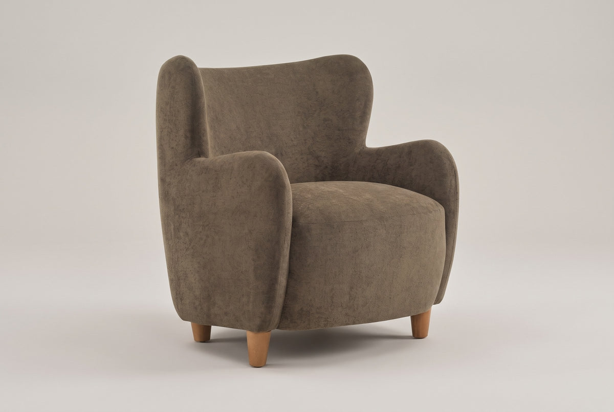 Bormio velvet wingback chair in dark brown, three-quarter view on a warm grey studio backdrop