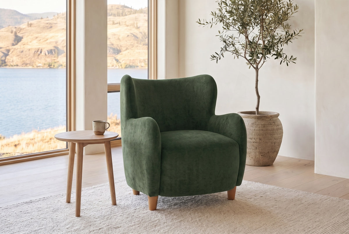 Bormio chair in olive green velvet beside a pale oak side table in a bright lake-house living room with an olive tree