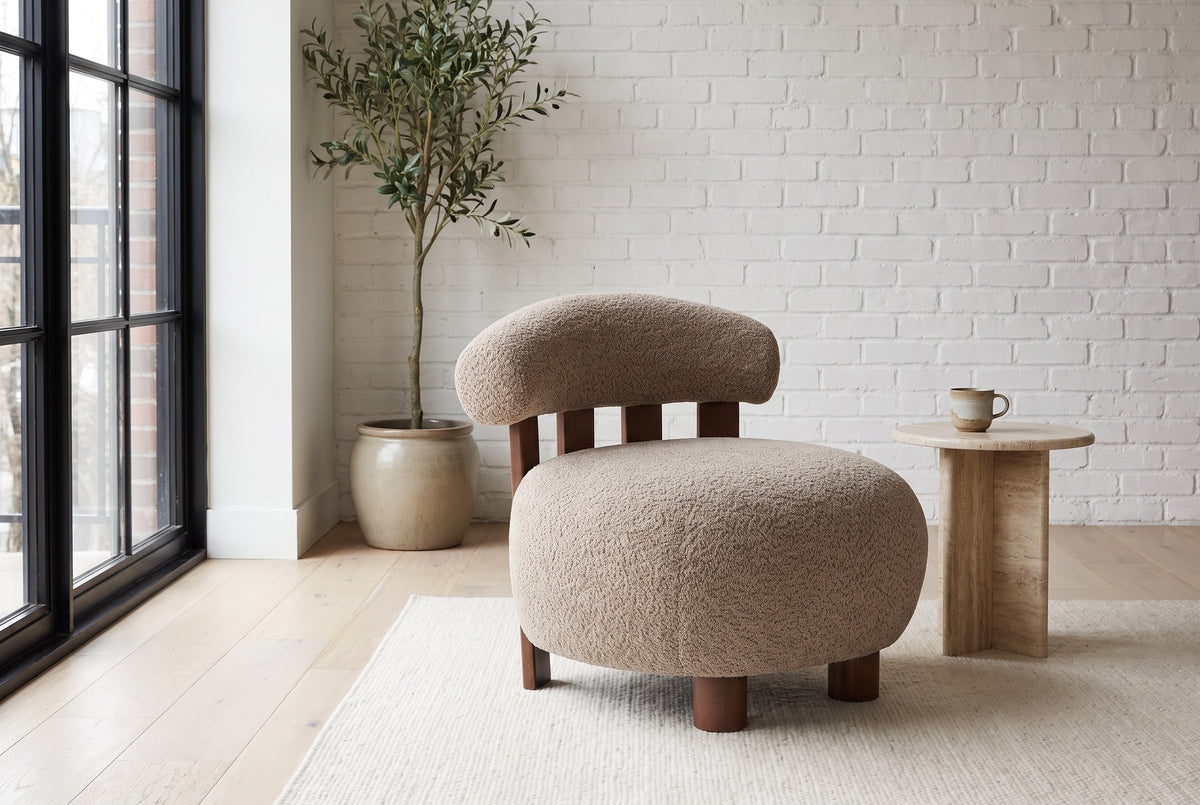 Brescia boucle accent chair in a white-brick loft with a travertine side table, an olive tree and a black steel window
