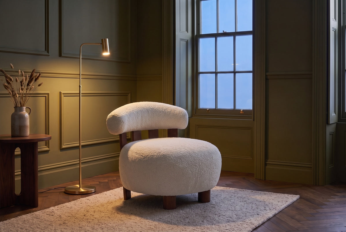 Brescia boucle accent chair in an olive-green panelled sitting room at dusk beside a lit brass floor lamp (Off White)