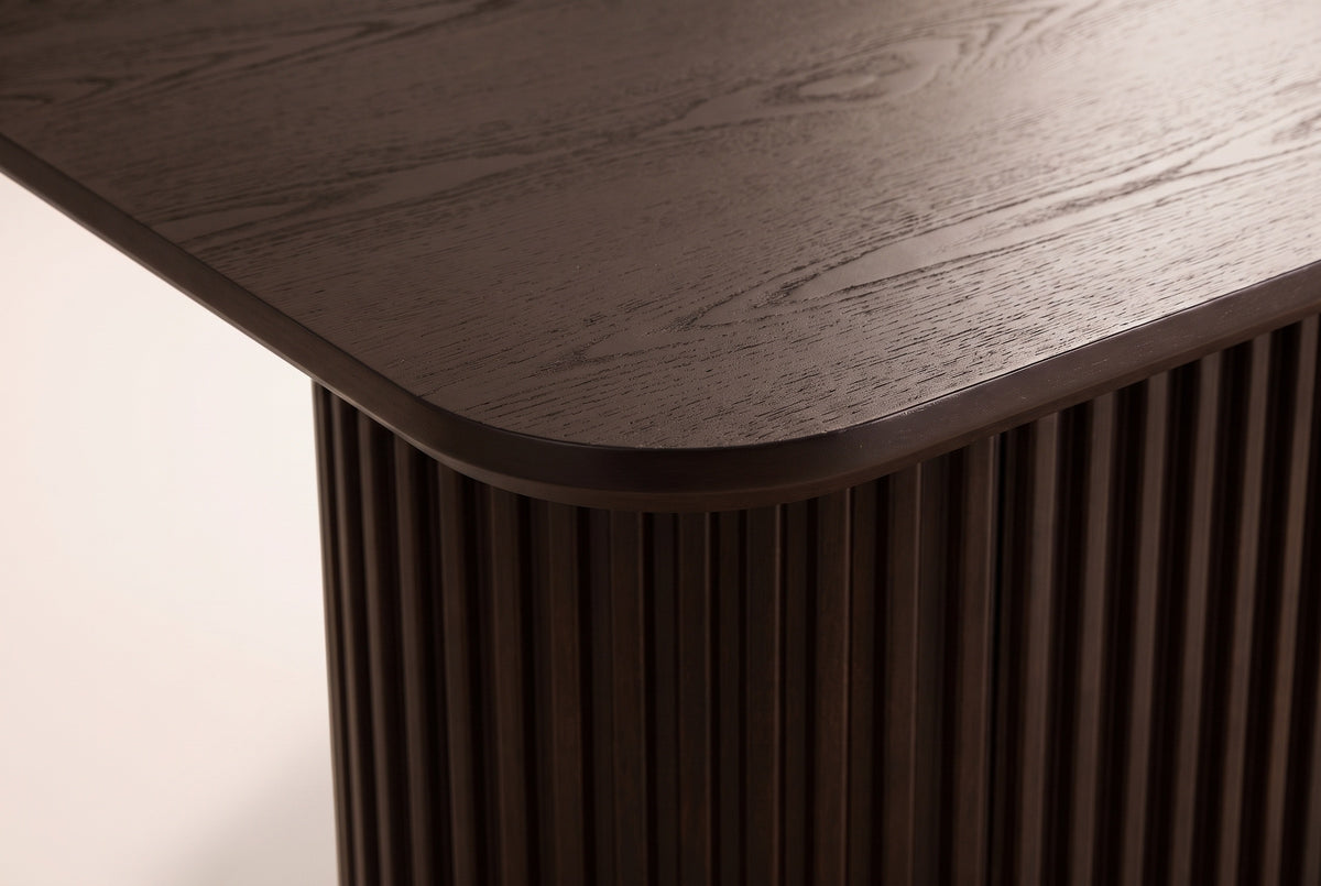 Close-up of the walnut open-grain top: a softly rounded corner, a slim edge and the fluted pedestal below