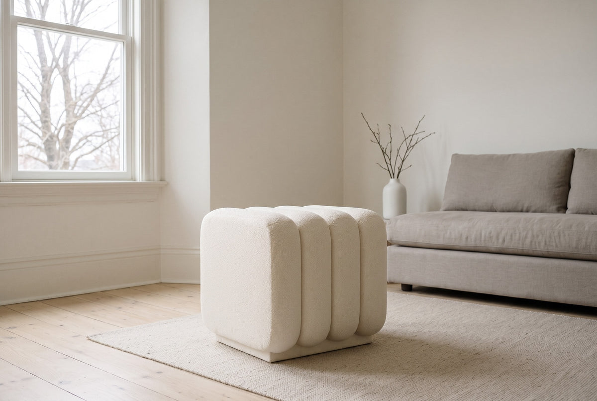 Brusson channel cube ottoman in cream boucle on an oatmeal rug in front of a grey linen sofa in a plaster living room in Halifax, a bare maple through the sash window
