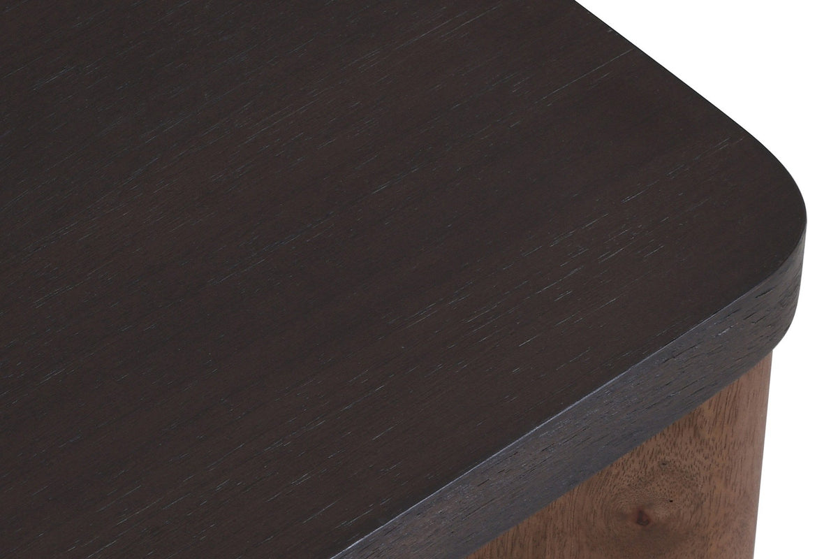 Close-up of the Calcata coffee table top: the mocha mango veneer, its rounded corner and edge band over a walnut leg