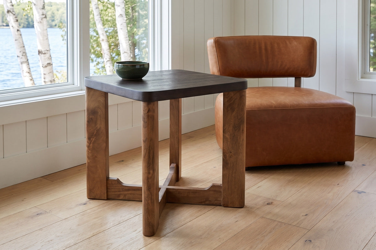Calcata side table beside a cognac leather chair in a Muskoka cottage, birch trees and the lake outside