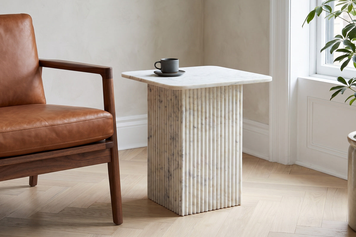 Camerota white marble side table beside a cognac leather lounge chair in a Montreal reading corner, a stoneware cup on top