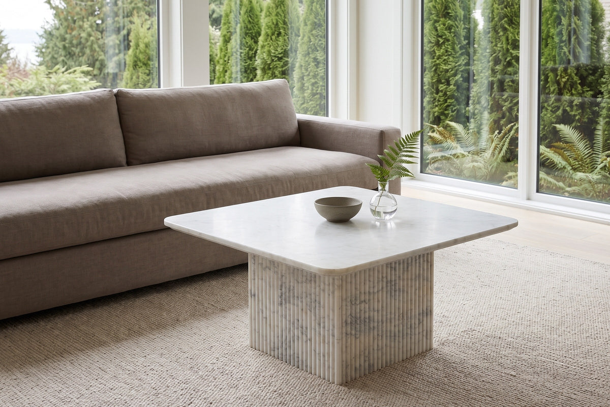 Campiglia white marble coffee table in front of a taupe linen sofa in a West Vancouver living room, cedars and ferns outside