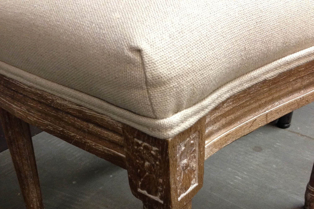 Close-up of a Candelo front corner: the piped linen seat, the moulded oak rail, a carved corner block and the fluted leg