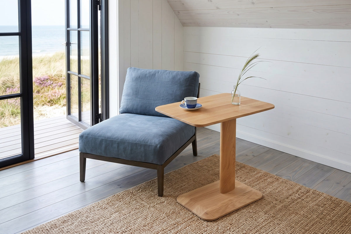 Capalbio side table in Natural seen from above beside a blue linen lounge chair in a house by the dunes