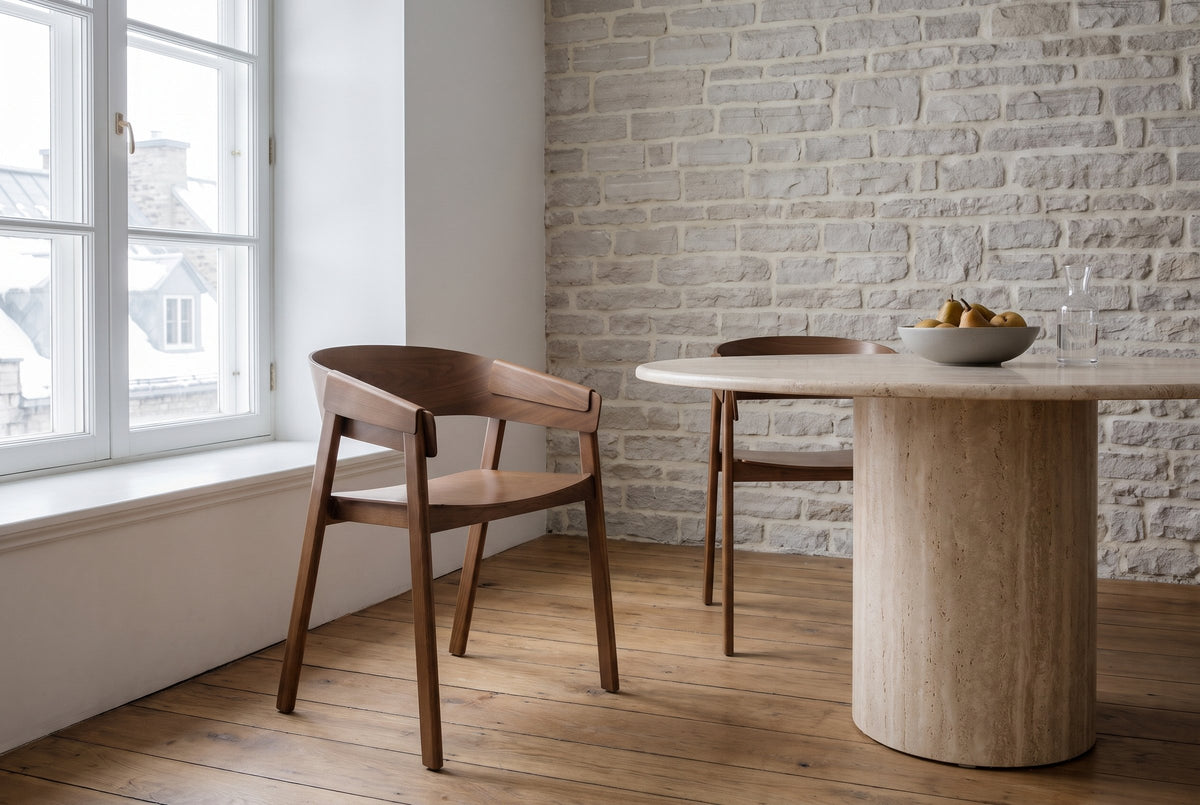 Two Caprarola dining armchairs in walnut at a round travertine pedestal table in a Quebec City stone house