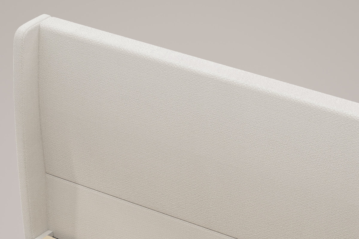Close-up of the Carrara headboard: the rounded top of a wing, the beige chenille and the one channel line
