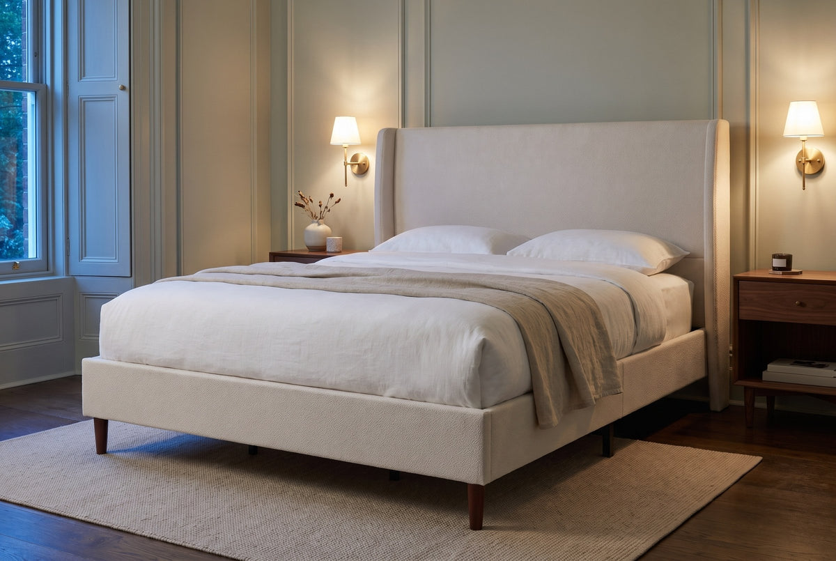 Carrara wingback bed in a sage-grey panelled bedroom at dusk, with brass sconces lit above walnut nightstands