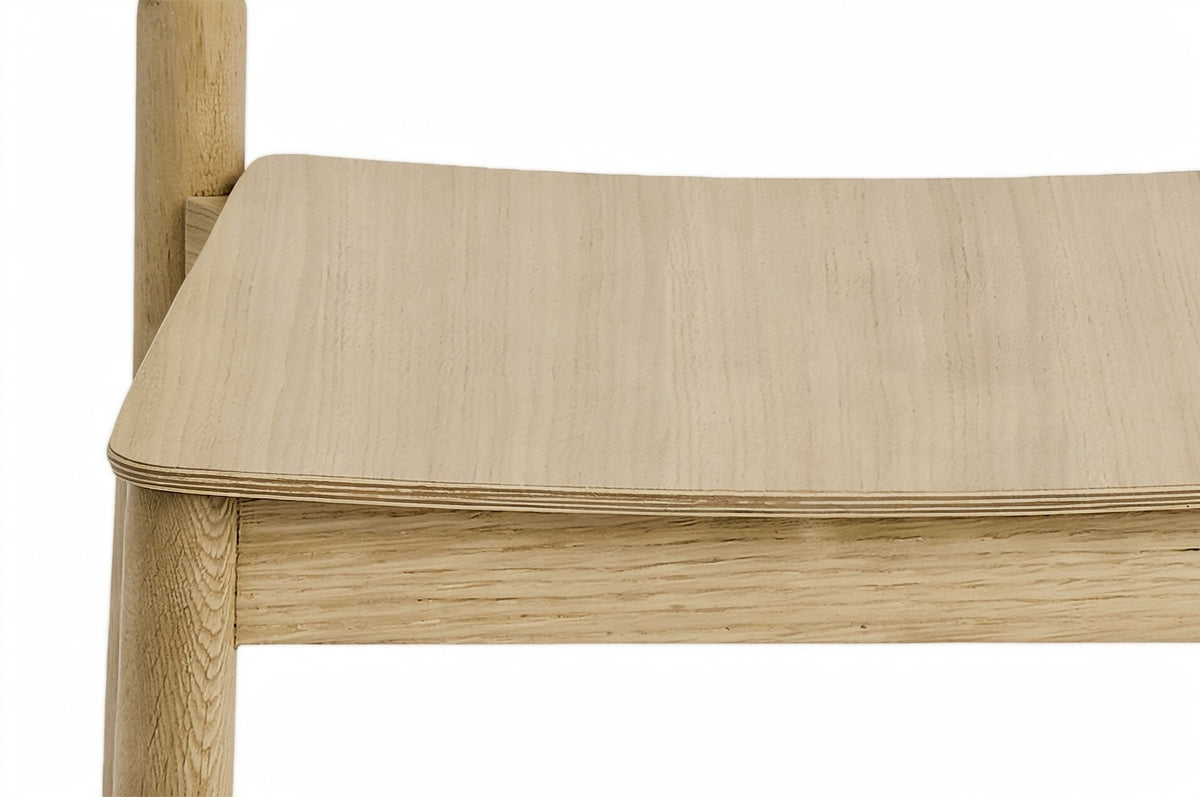 Close-up of the Casole seat corner in natural oak: the rounded plywood edge over the apron and the top of a round leg