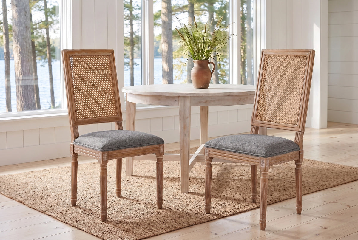 A pair of Castelfranco dining chairs in Mid Grey on a jute rug in a white Muskoka cottage with a round table and the lake beh