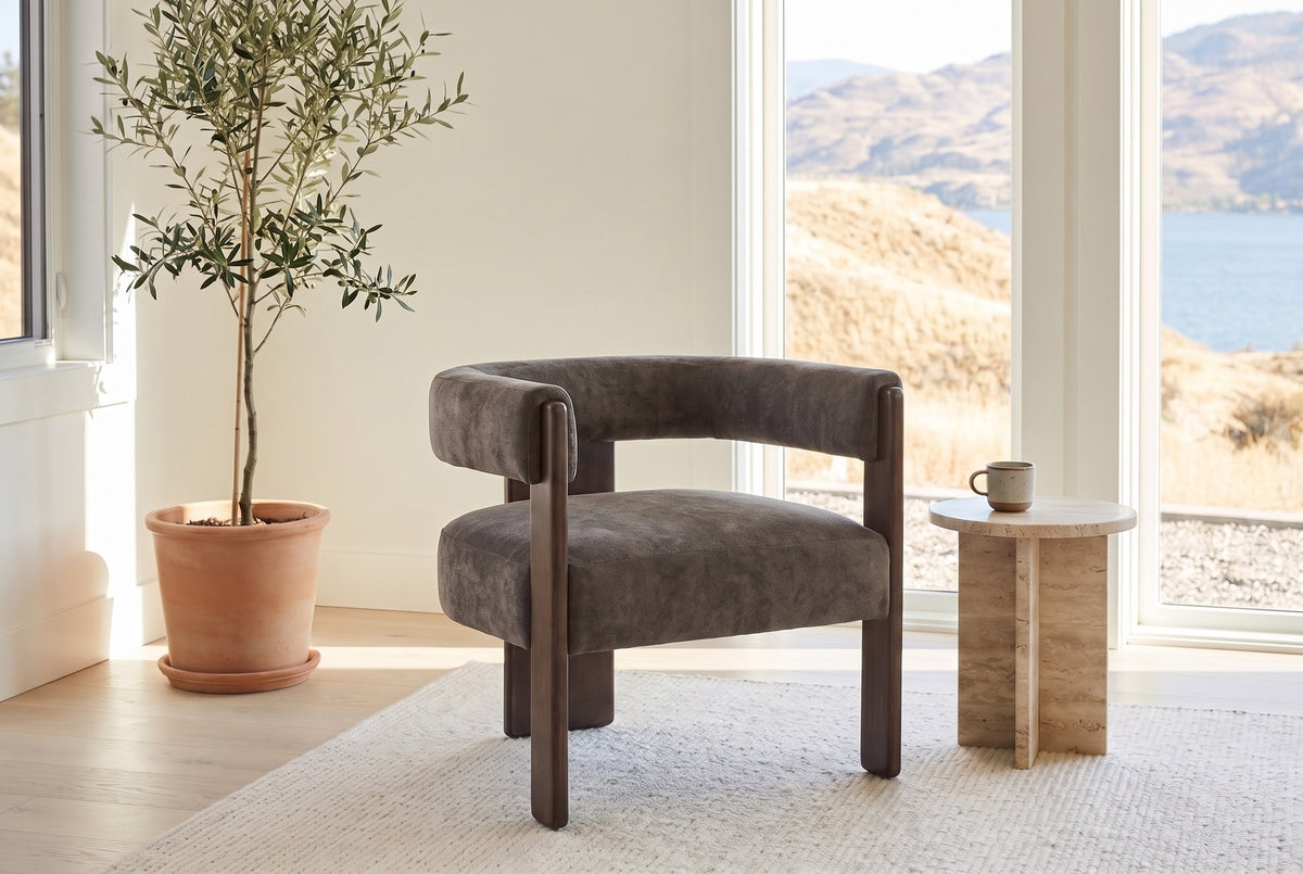 Chioggia accent chair in Dark Brown by a lake-view window with a travertine side table and an olive tree