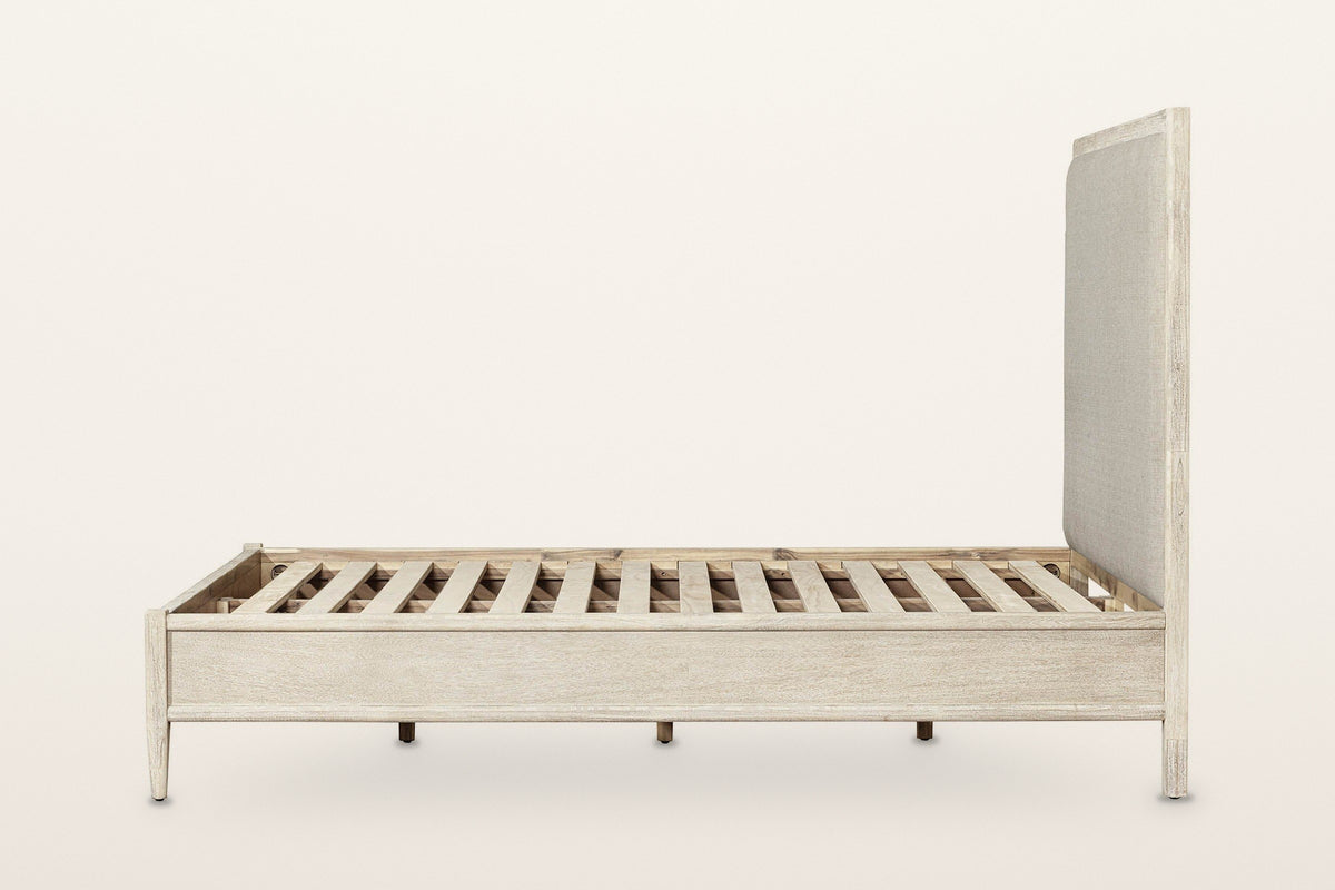 Side view of the Chiusdino bed on a warm white studio backdrop: the low moulded side rail, the tapered foot leg