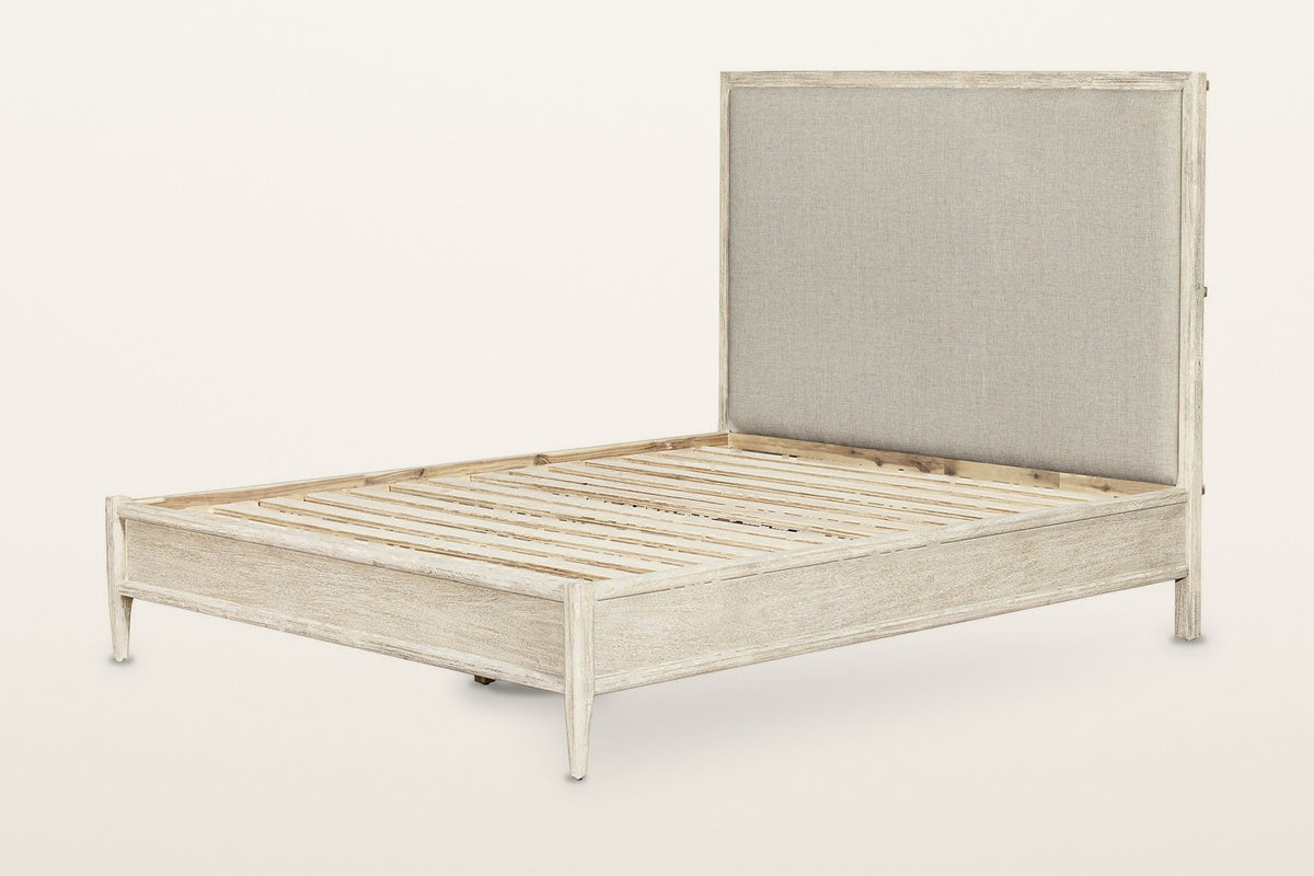 Chiusdino bed frame in whitewashed wood, three-quarter view on a warm white studio backdrop: a tall greige linen-look headboa