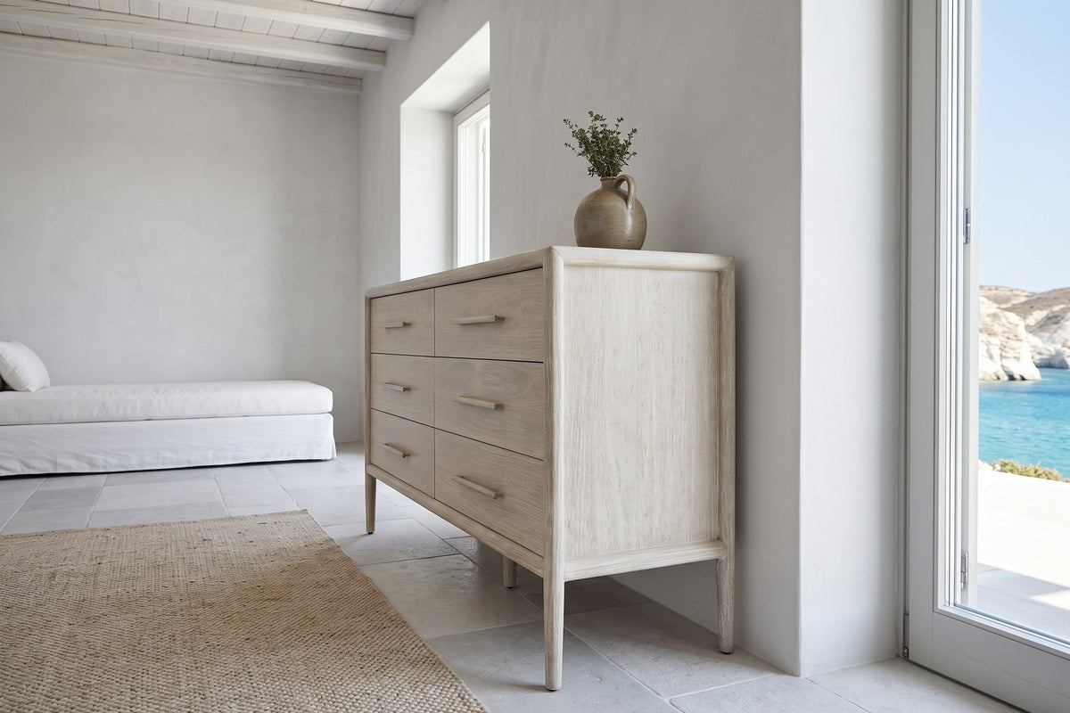 Low side view of the Chiusdino dresser in a pale whitewashed finish in a white Milos cliff house, with a linen daybed