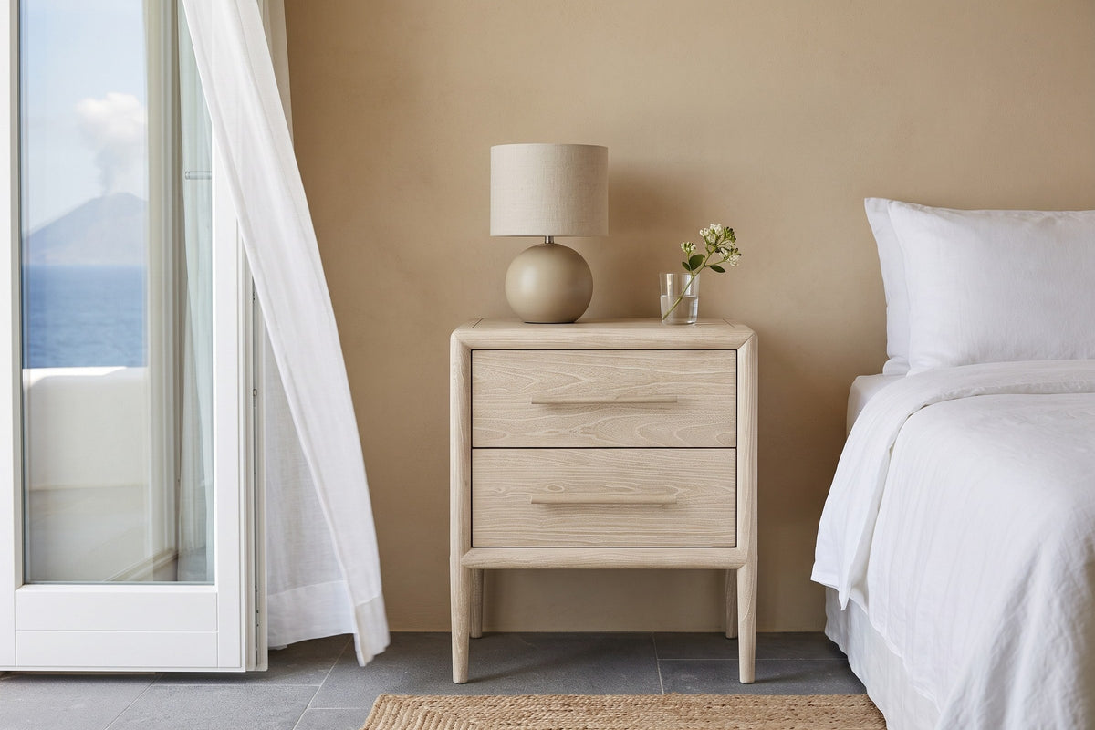 Chiusdino nightstand in whitewashed wood beside a white linen bed in a Panarea villa bedroom, with sand lime plaster