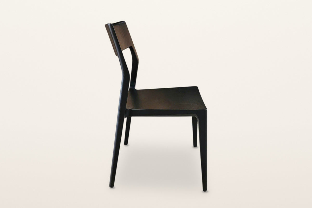 Cison dining chair in Black, side view on a warm white studio backdrop: the back post leans back and runs down into the rear