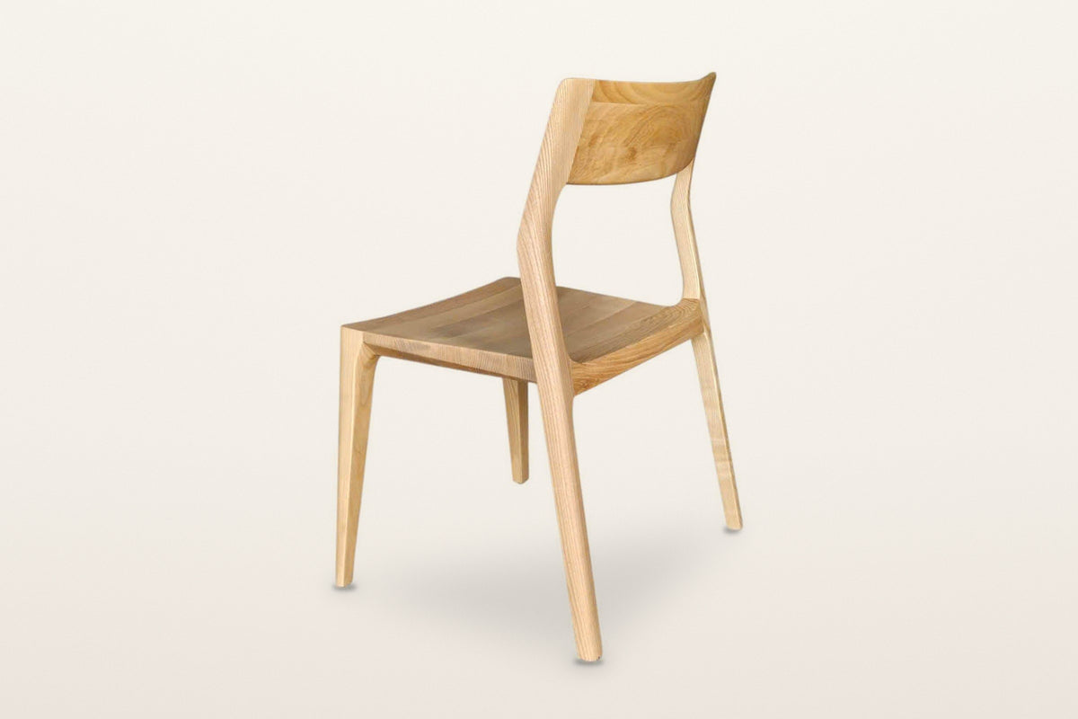 Cison dining chair in Natural, rear three-quarter view on a warm white studio backdrop: the back of the backrest and the open