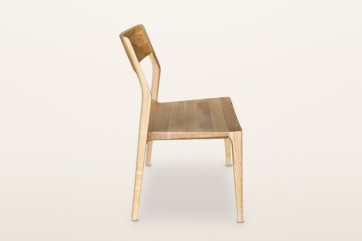 Cison dining chair in Natural, side view on a warm white studio backdrop: the back post leans back and runs down into the rea