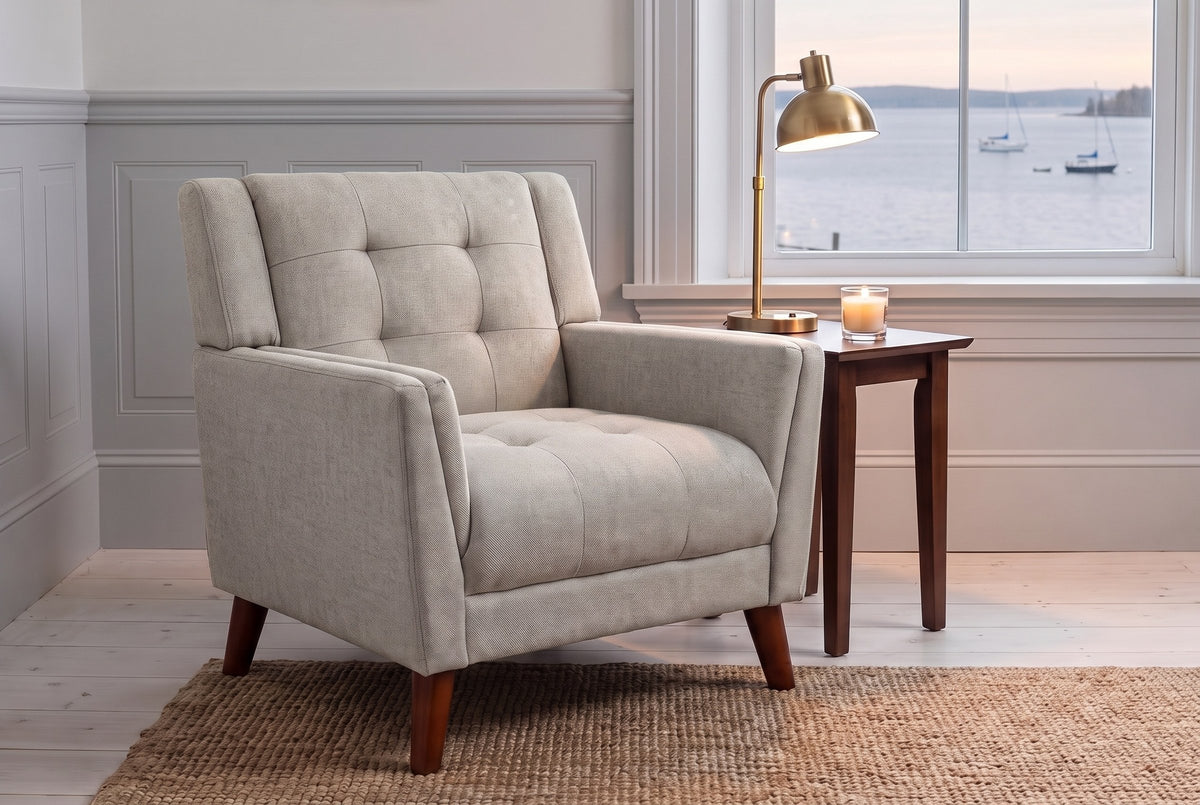 Comacchio armchair in beige by a harbour window at dusk, a brass lamp lit on a walnut side table
