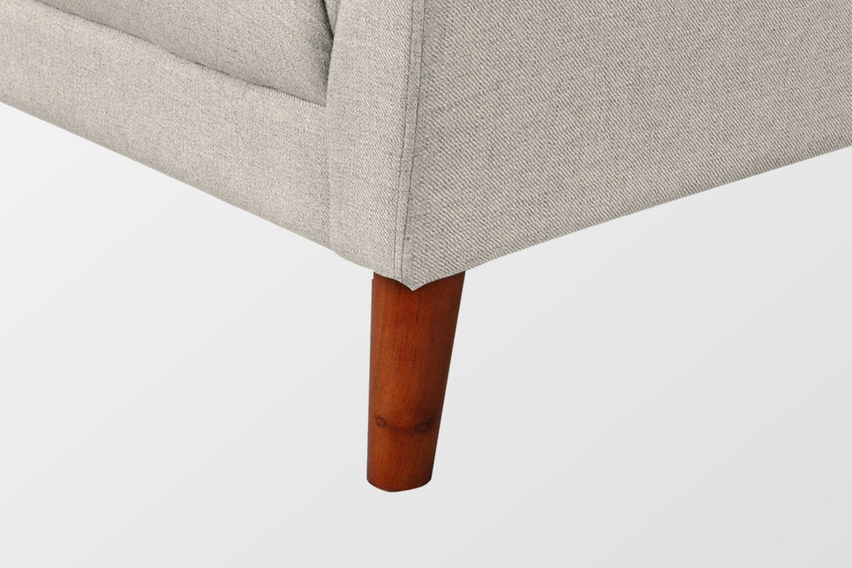 Close-up of the beige front corner and a tapered solid wood leg in a walnut finish