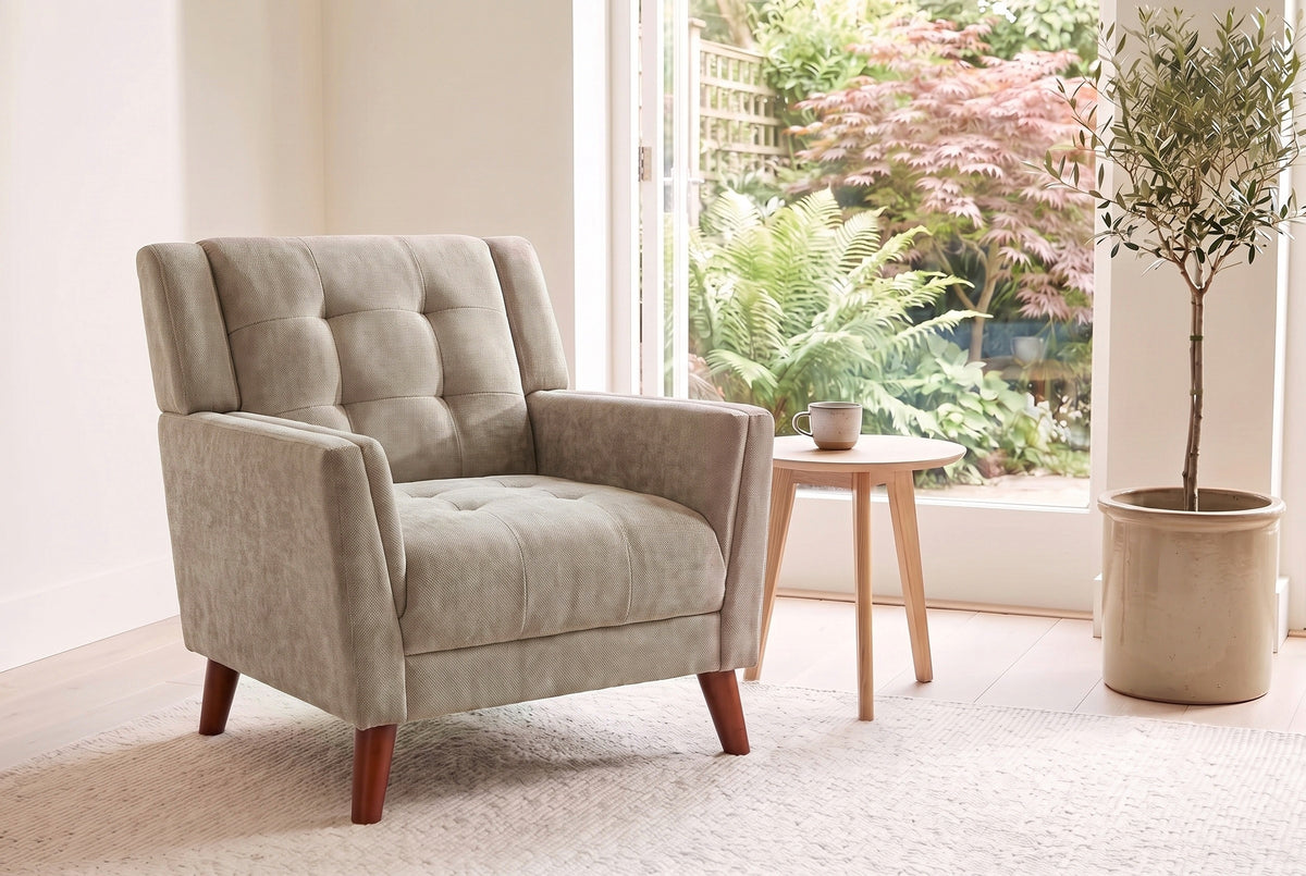 Comacchio armchair in light brown beside a pale oak side table in a bright garden room with ferns and an olive tree