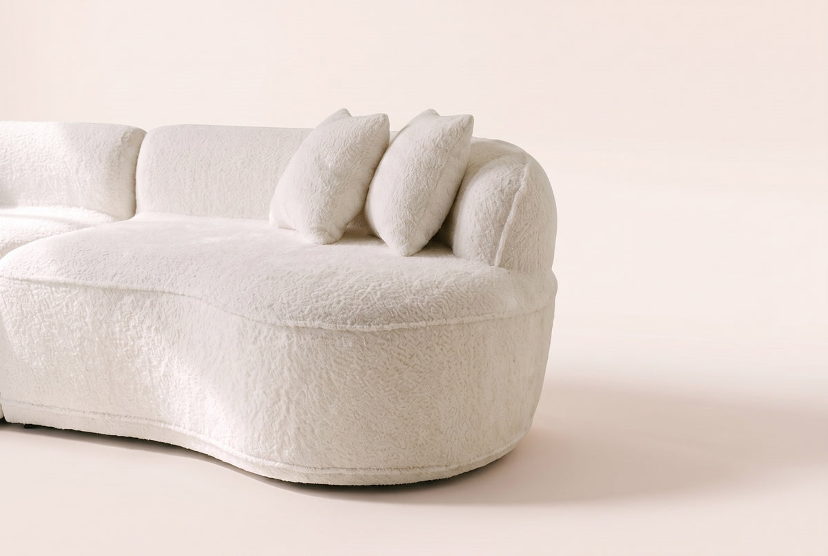 Close-up of a rounded end of the Fiora sofa in White, curly ivory boucle and throw pillows