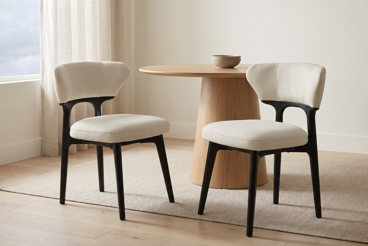 Two Fosdinovo dining chairs pulled out from a round oak table in a bright Vancouver apartment with a linen curtain