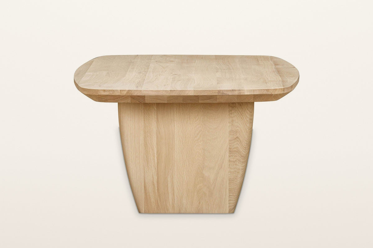 Frontino coffee table in Biscotti Oak from the end on a warm white studio backdrop: a slab leg wide under the top