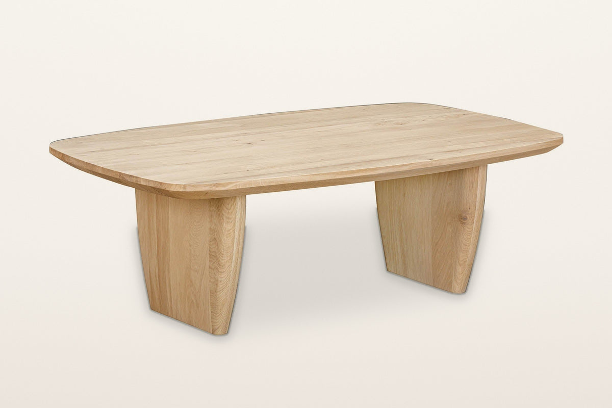 Frontino oak coffee table in Biscotti Oak, three-quarter view on a warm white studio backdrop: a soft boat-shaped top on two