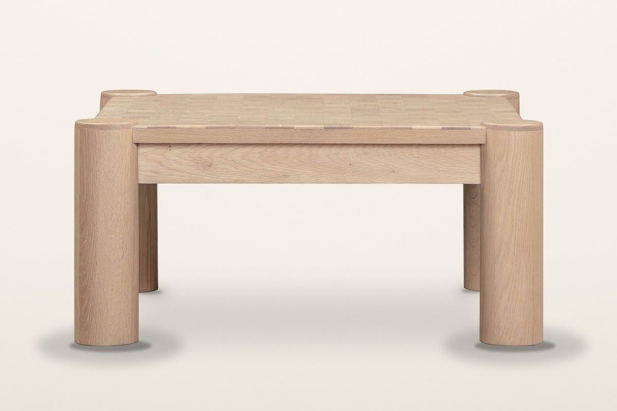 Furore coffee table in Biscotti Oak from the front on a warm white studio backdrop: two column legs and the set-back apron