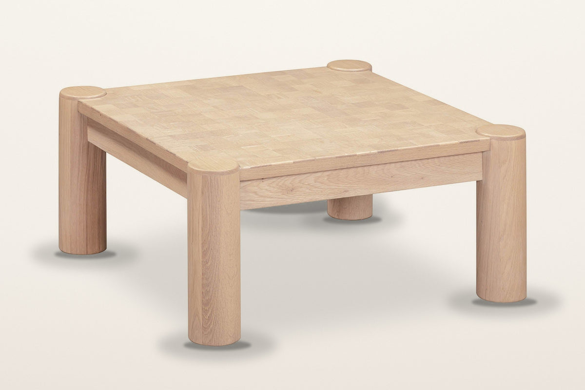 Furore oak coffee table in Biscotti Oak, three-quarter view on a warm white studio backdrop: a square parquet top on four rou